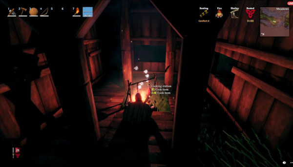 Player character sitting inside a dim, wooden hut, warming up by a campfire on the floor.